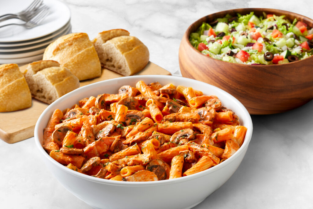 A bowl of rigatoni with a salad and bread