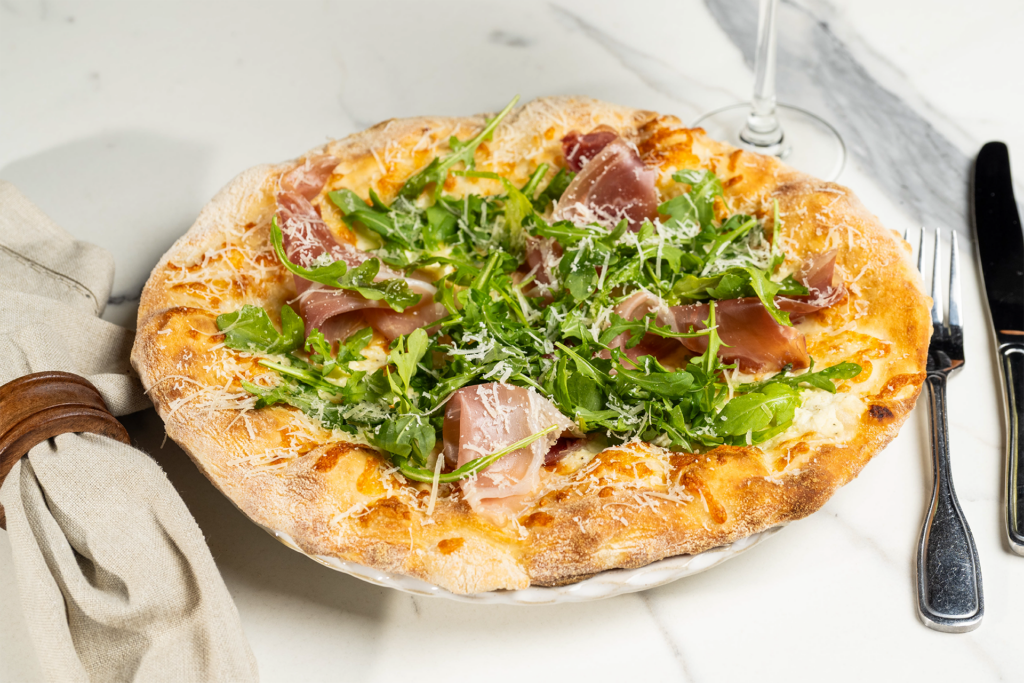 Prosciutto and arugula pizza topped with grated cheese.