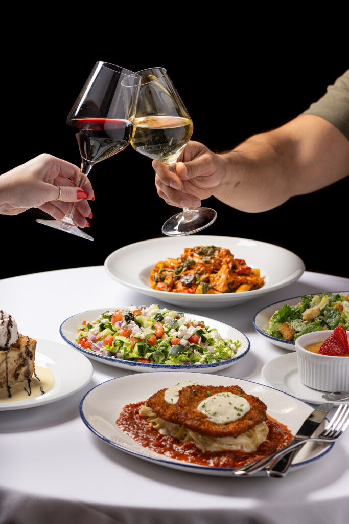 Two people clinking wine glasses together over Chicken Milanese with Salad and Crème Brûlée
